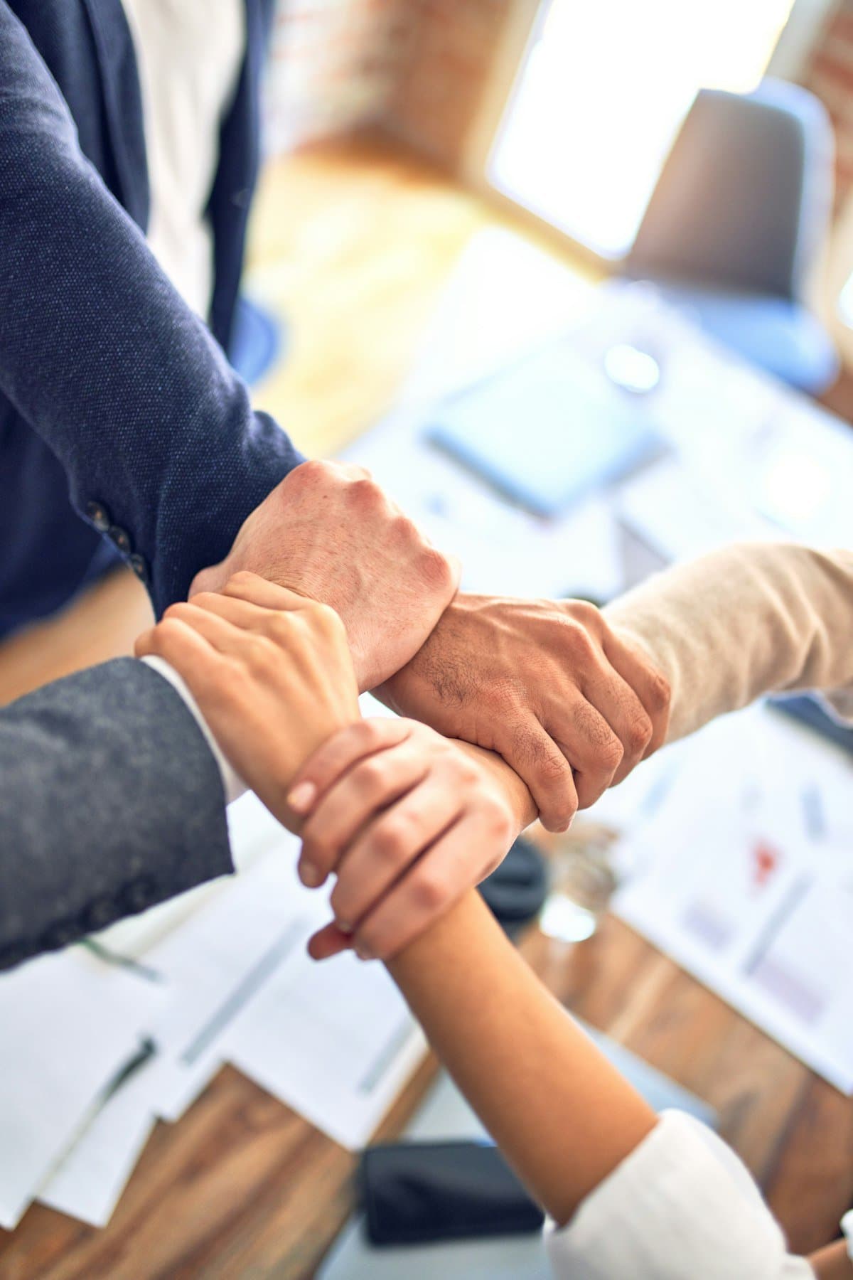Four colleagues joining hands over a desk of work in progress